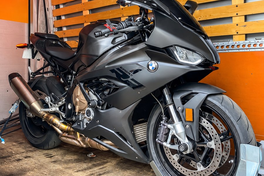 Moto sportive calée sur sa roue avant dans un camion fermé, cloison bois et rail d’arrimage